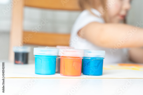 set of gouache in jars placed on a table for children's creativity. In the background a child in blur. activities with the child in isolation and quarantine in connection with the coronavirus