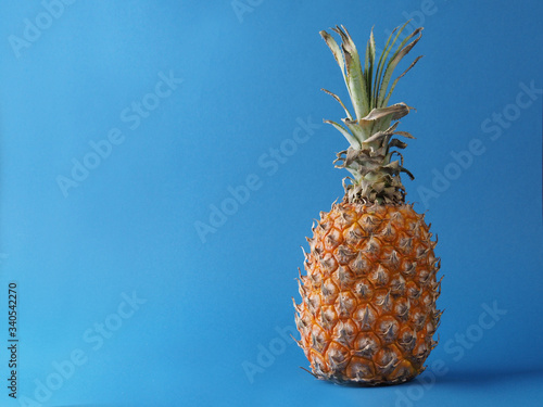 Ripe orange pineapple with green leaves on a blue background.
