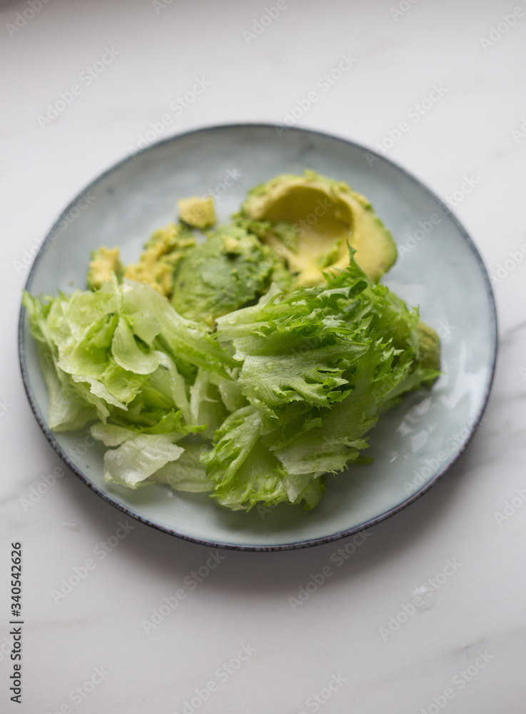 lettuce and avocado in rustic plate on white marble background lettuce and avocado in rustic plate on white marble background