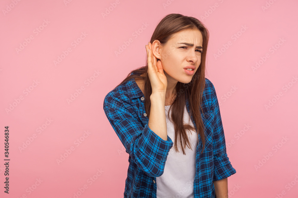 What? Repeat I don't hear! Portrait of girl in checkered shirt keeping hand near ear, listening to secret rumor with concentrated attentive expression. indoor studio shot isolated on pink background What? Repeat I don't hear! Portrait of girl in checkered shirt keeping hand near ear, listening to secret rumor with concentrated attentive expression. indoor studio shot isolated on pink background