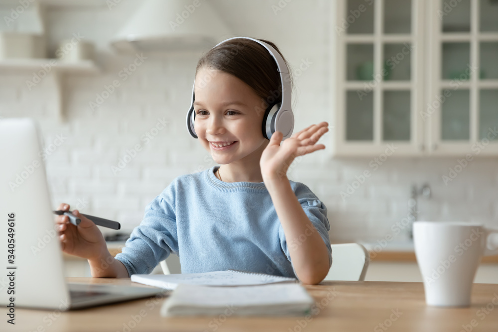 Smiling little Caucasian girl in headphones have video call distant class with teacher using laptop, happy small child wave greeting with tutor, study online on computer, homeschooling concept Smiling little Caucasian girl in headphones have video call distant class with teacher using laptop, happy small child wave greeting with tutor, study online on computer, homeschooling concept