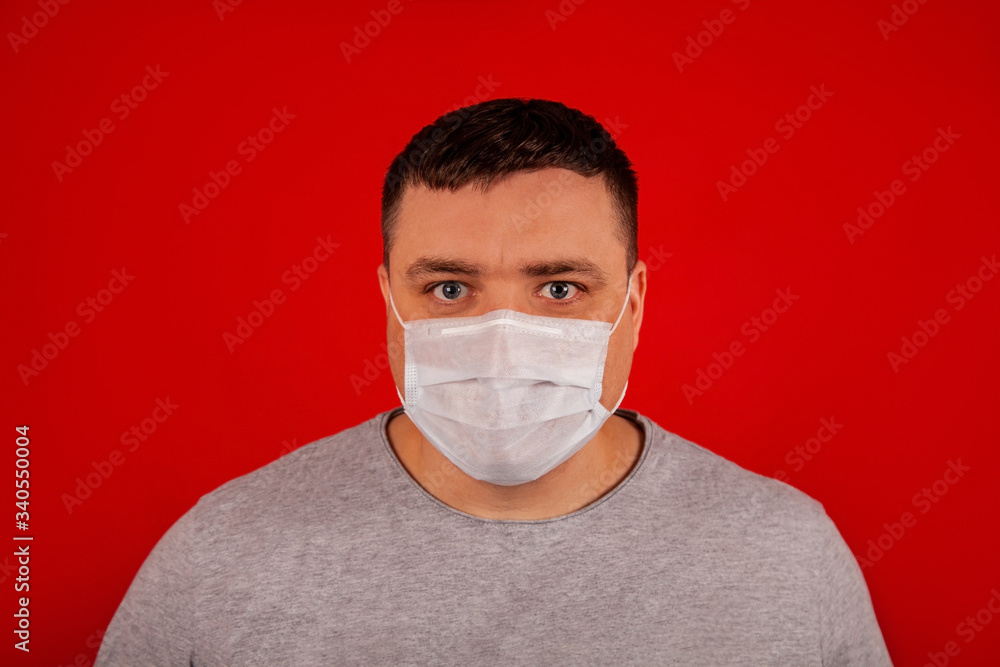 Portrait of a young man looking at the camera in a medical protective mask on a red background Portrait of a young man looking at the camera in a medical protective mask on a red background