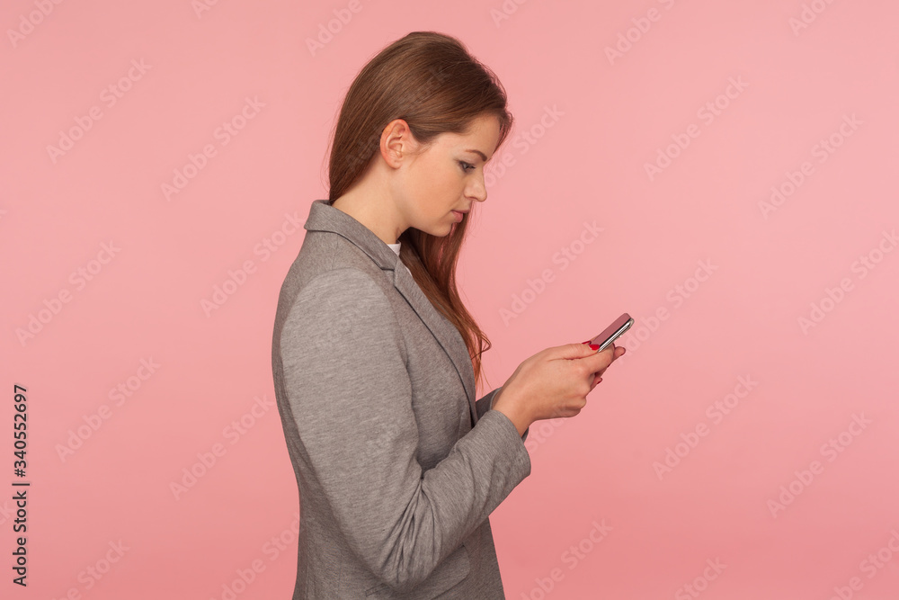 Mobile business apps. Side view of serious focused elegant lady boss in suit reading message, checking news on smartphone, using online services. indoor studio shot isolated on pink background Mobile business apps. Side view of serious focused elegant lady boss in suit reading message, checking news on smartphone, using online services. indoor studio shot isolated on pink background