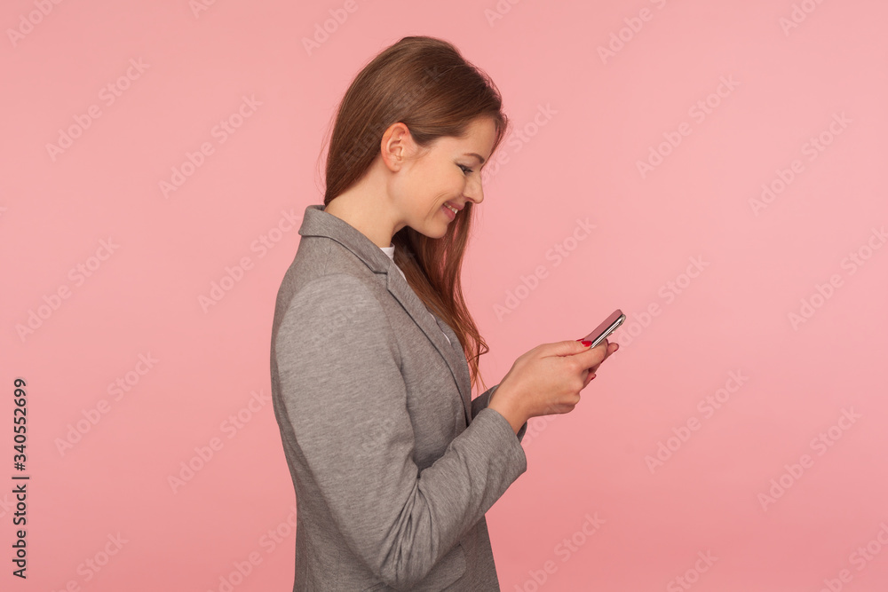 Mobile business application. Side view of satisfied and smiling elegant lady boss in suit reading positive message, checking good news on smartphone, using online services. studio shot, isolated Mobile business application. Side view of satisfied and smiling elegant lady boss in suit reading positive message, checking good news on smartphone, using online services. studio shot, isolated