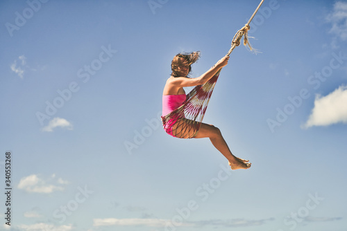 Caucasian girl in pink swimsuit swinging on the beach at El Nido, Philippines on a sunny day with clouds.