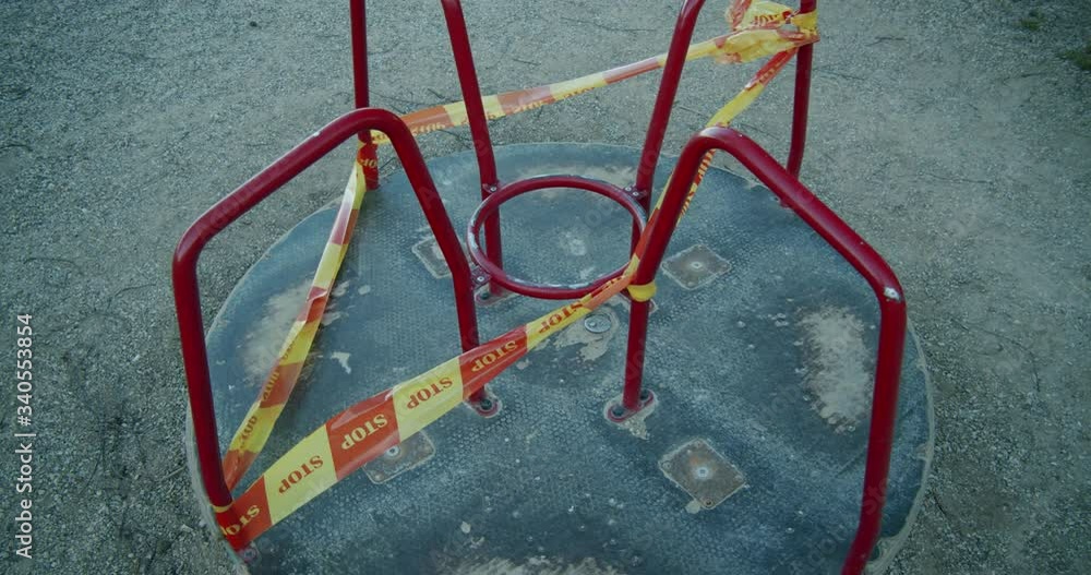 A Slowly Moving Closed Down Merry Go Round Swing in an Empty Kids' Playground Wrapped in Yellow and Red A Slowly Moving Closed Down Merry Go Round Swing in an Empty Kids' Playground Wrapped in Yellow and Red