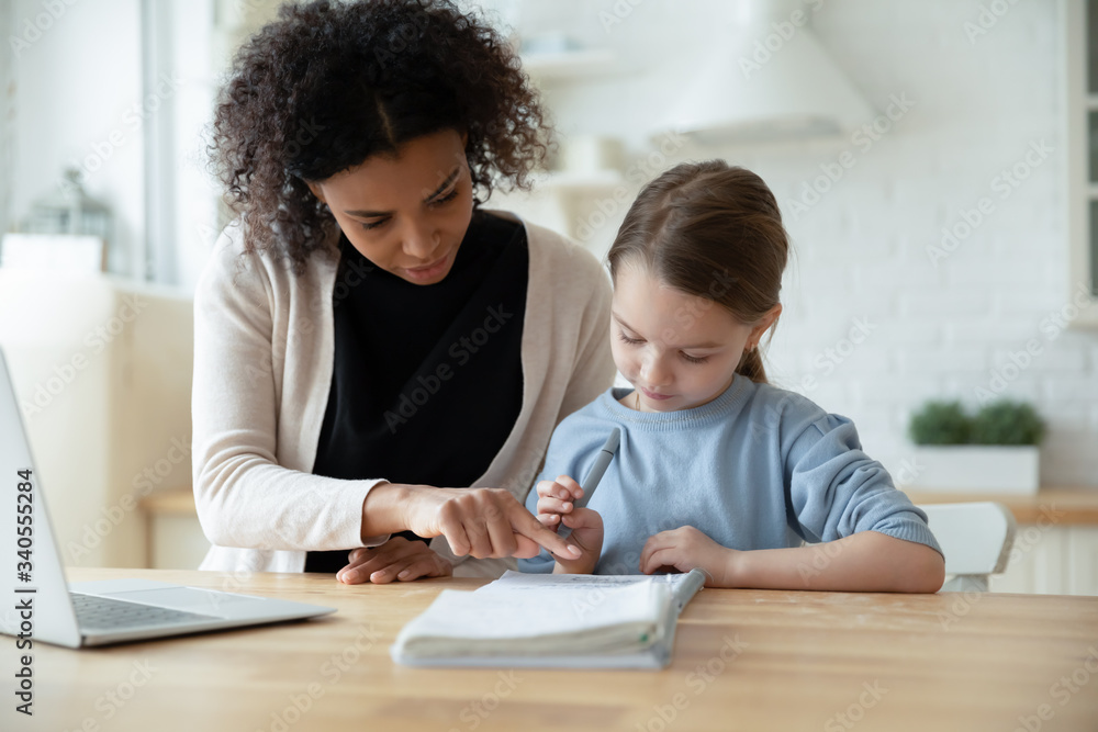 Caring African American mom help little Caucasian daughter studying together online at home, biracial mother teach learn with European girl child, have internet web class, homeschooling concept Caring African American mom help little Caucasian daughter studying together online at home, biracial mother teach learn with European girl child, have internet web class, homeschooling concept
