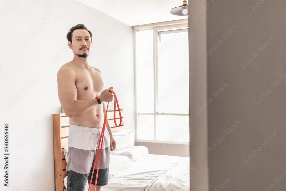 Obraz premium Asian man stretching his muscle in concept of workout at home with resistance band.