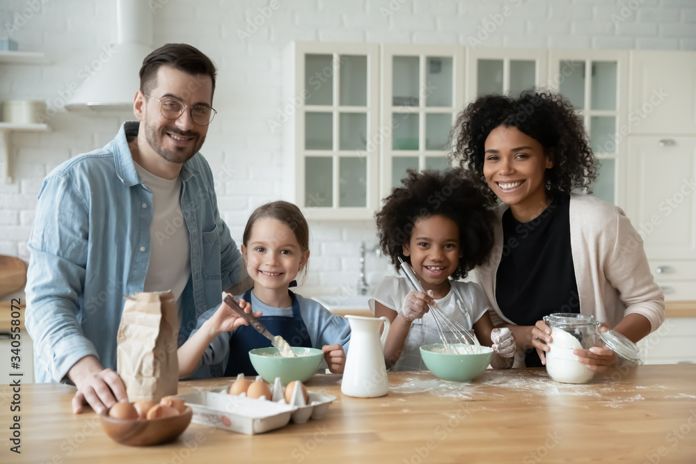 Portrait of happy young multiracial family with little daughters bake biscuits in kitchen together, smiling parents with small multinational daughters children have fun cooking breakfast at home Portrait of happy young multiracial family with little daughters bake biscuits in kitchen together, smiling parents with small multinational daughters children have fun cooking breakfast at home