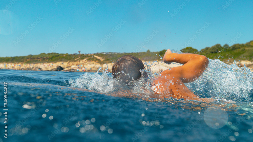CLOSE UP: Young male tourist goes for a swim to cool off on a sunny summer day.