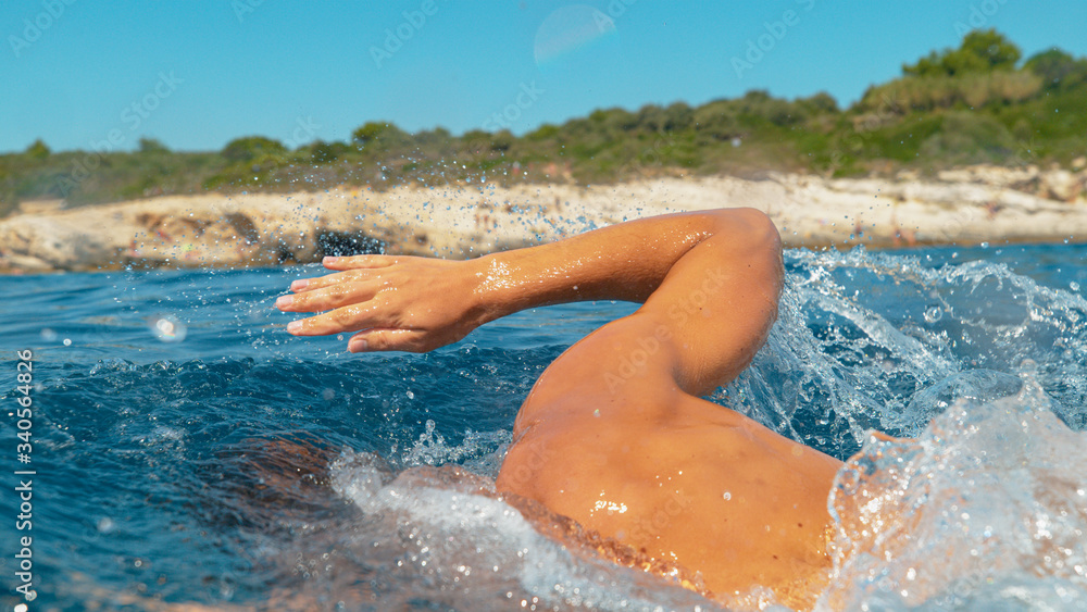 CLOSE UP: Unrecognizable athletic man swims in the sea on a sunny summer day.