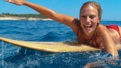 PORTRAIT: Smiling surfer girl having fun swimming to the line up to catch waves. © helivideo