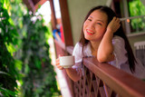 young happy and beautiful Asian Korean woman having morning coffee or tea at hotel terrace or home balcony leaning on the balustrade relaxed and cheerful