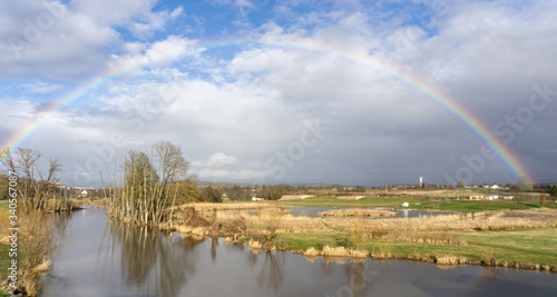 Feld entlang der Mainaue (Fluss) mit Regenbogen vor blauem Himmel leuchtet über dem Panorama. Mainaue. Bayreuth. Deutschland.