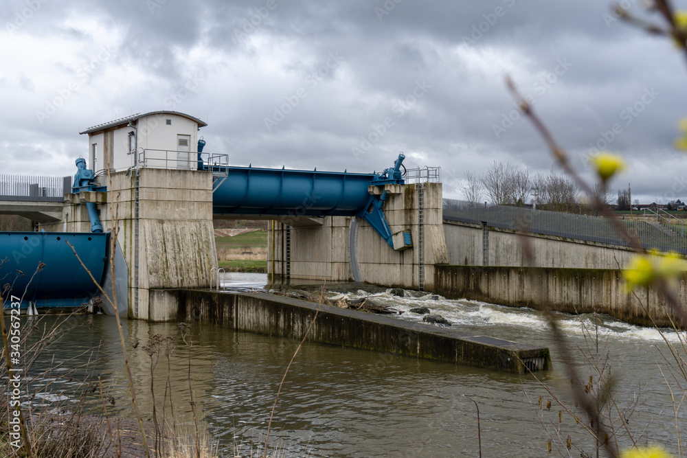 Staudamm mit blauen Auffangbehältern im Wasser bei bewölktem Himmel. Bayreuth. Mainaue. Detail. Staudamm mit blauen Auffangbehältern im Wasser bei bewölktem Himmel. Bayreuth. Mainaue. Detail.