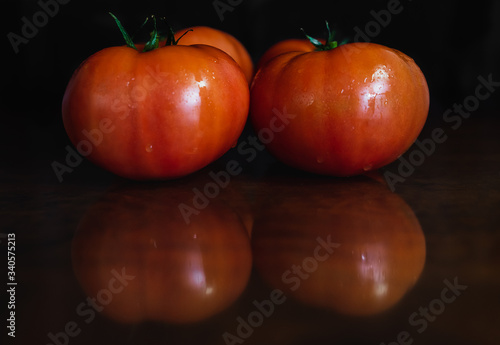 Red tomatoes on a dark wooden surface where are reflected