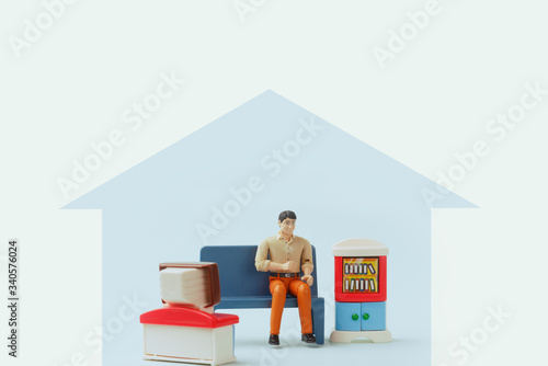 Stay home awareness social media campaign and coronavirus prevention: man sitting on the sofa and watching tv. Toy figure of a man in a doll house. Quarantine, self-isolation social distance concept.