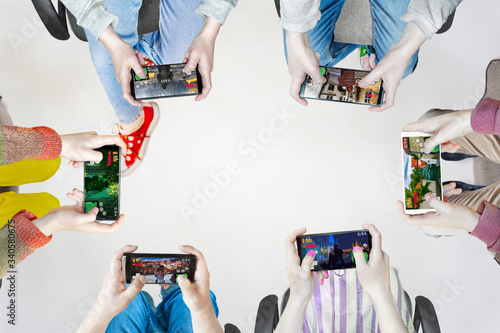 Hands of people playing multiplayer online games with friends on phones while sitting in a bright room. Phone screens are isolated in color. In the center is an empty place for inscriptions.