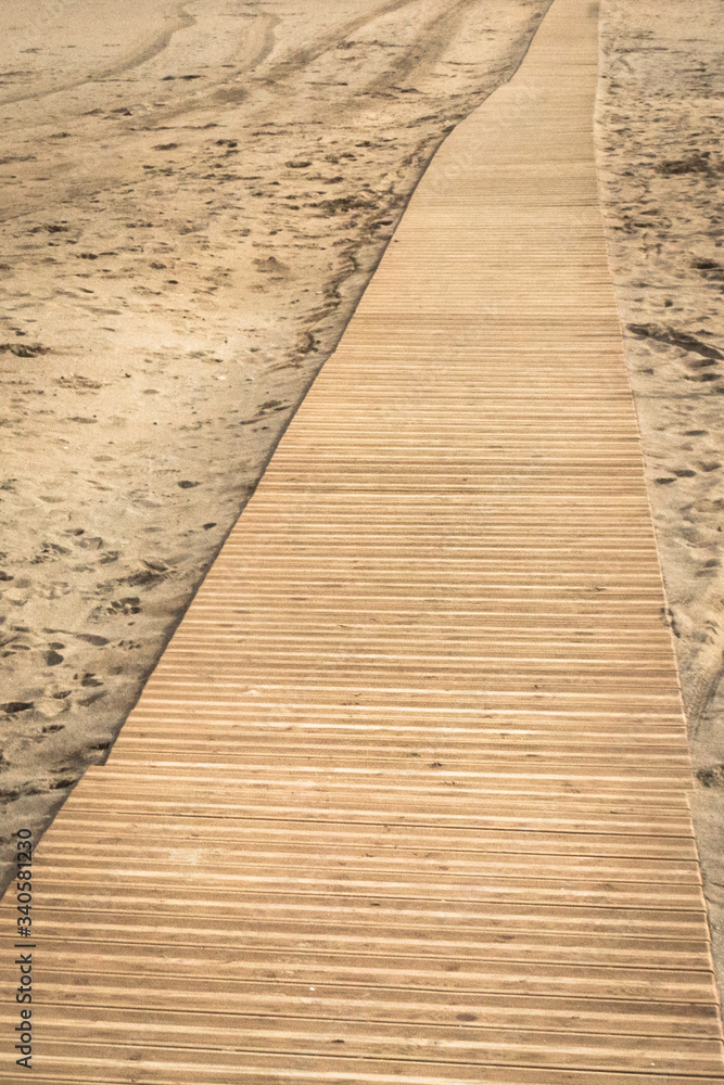 Boardwalk through the sand. Relax on the sandy beach. Holidays at sea. Walk in the fresh air. Sea air. Wooden path through the sandy beach. The texture of sand and boards.