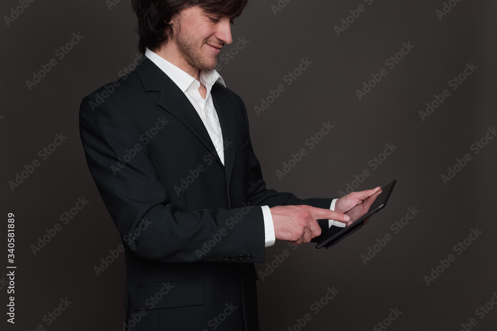 Businessman in black suit holding tablet pc in his hand side view. Touching screen with index finger Businessman in black suit holding tablet pc in his hand side view. Touching screen with index finger