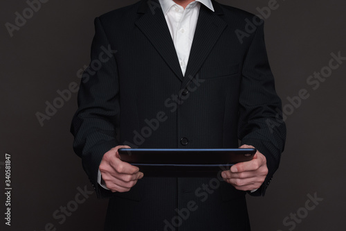 Businessman in black suit holding tablet pc in his hands closeup front view. Two hands holding device