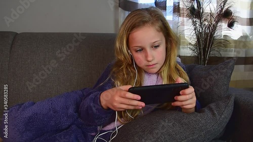 Cute girl of 9 years old lies on the couch in her pajamas, plays with the phone