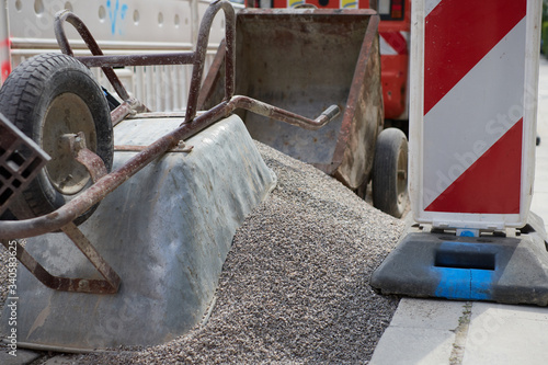 A wheelbarrow on a heap of gravel on a construction site in a city area delimited with safety markings