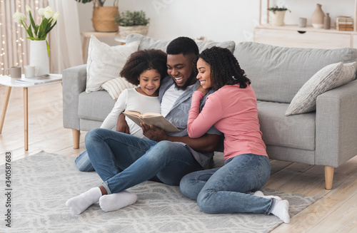 Happy black family reading book together, staying at home during quarantine