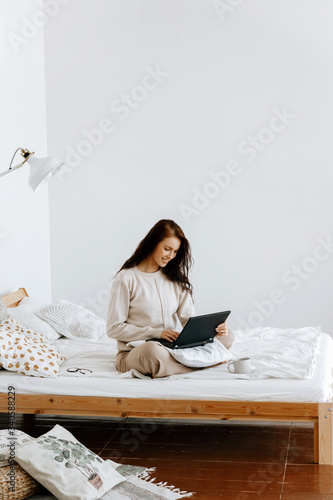 Distance learning or working from home concept. A young beautiful woman in beige home clothes is studying or working from home on a laptop in her bedroom via the Internet.