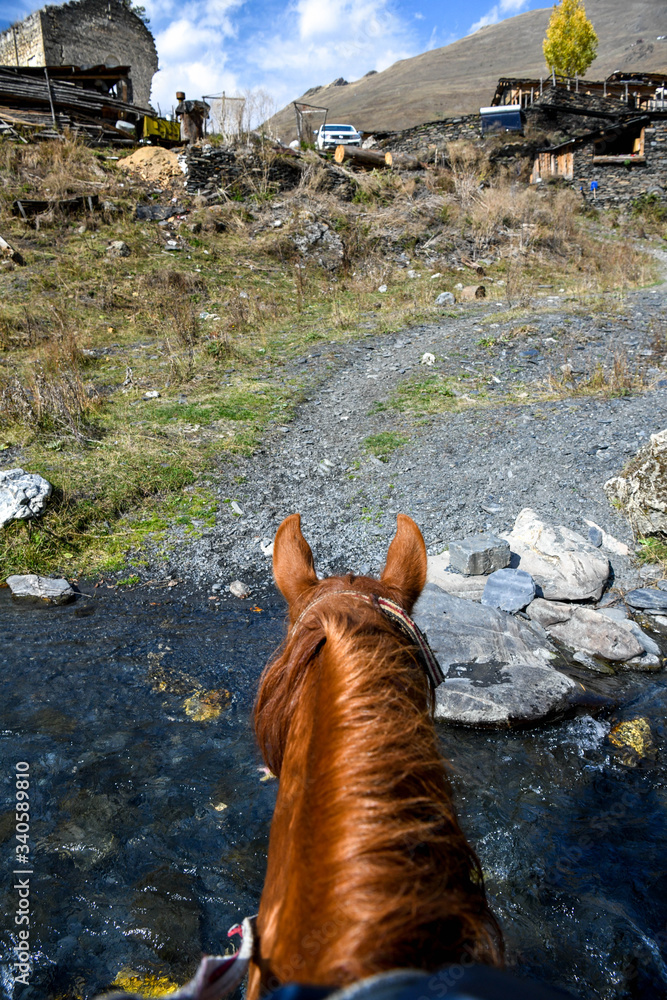 Obraz premium Rear view of a horse crossing a river to enter the village of Dartlo