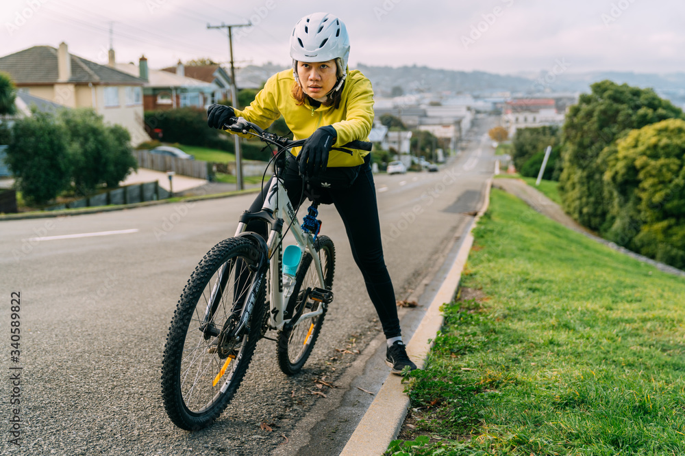 Fototapeta premium 18/04/2020 Asian woman making uphill with mountain bike. A woman very tired and stop on street At Oamaru, New Zealand.