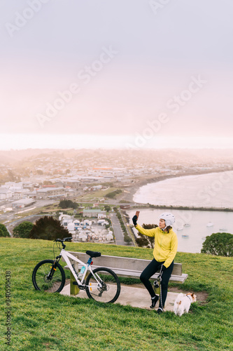 Asian woman making uphill with mountain bike. A woman taking a picture at lookout point with a dog at Oamaru, New Zealand.