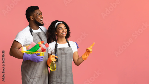 Smiling couple holding basket with detergents and pointing at copy space