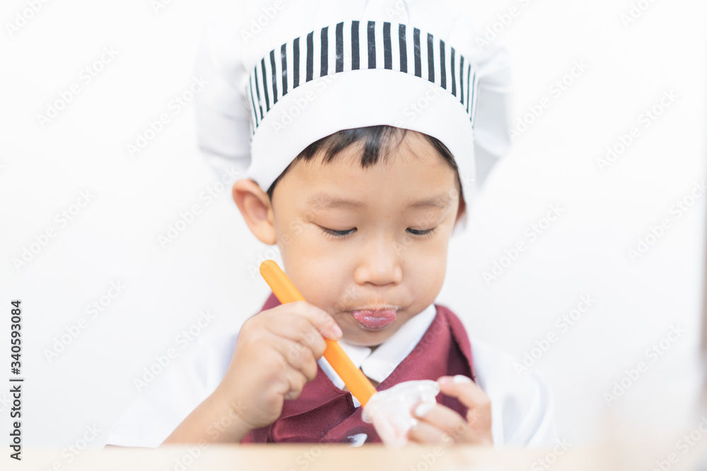 A little chef is eating yogurt. A little chef is eating yogurt.
