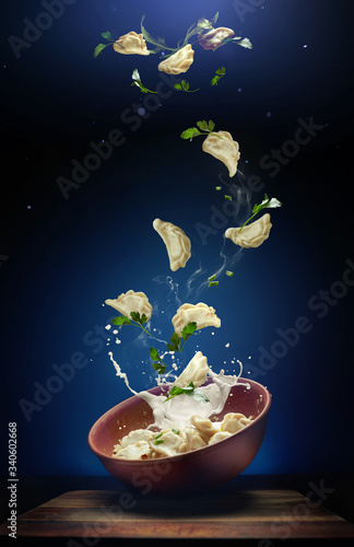 Hot pierogi flying out of the clay bowl with cream and parsley. Some vareniki stay inside the plate. Blue background.