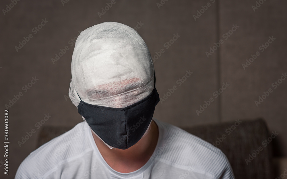 bandaged head of a bearded man. the head is wrapped in a gauze bandage. no eyes visible. medical black mask on the face. first aid at home. coronavirus, covid 19, quarantine, mummy bandaged head of a bearded man. the head is wrapped in a gauze bandage. no eyes visible. medical black mask on the face. first aid at home. coronavirus, covid 19, quarantine, mummy