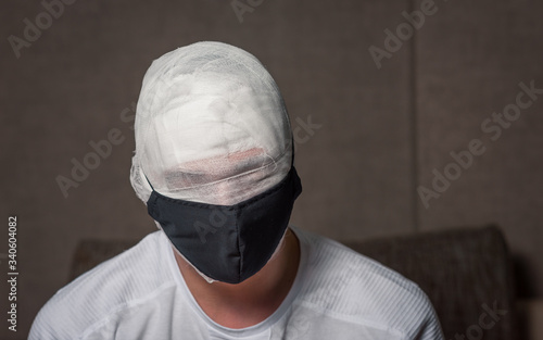 bandaged head of a bearded man. the head is wrapped in a gauze bandage. no eyes visible. medical black mask on the face. first aid at home. coronavirus, covid 19, quarantine, mummy © Evghenii Blanaru