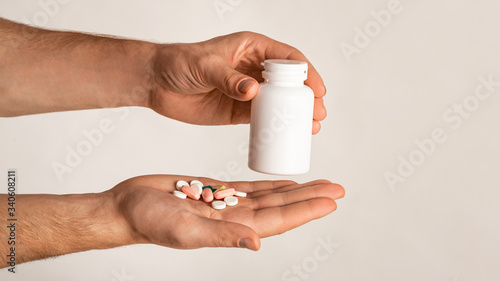 Unrecognizable guy holding bottle of meds and different pills on light background, space for design. Panorama