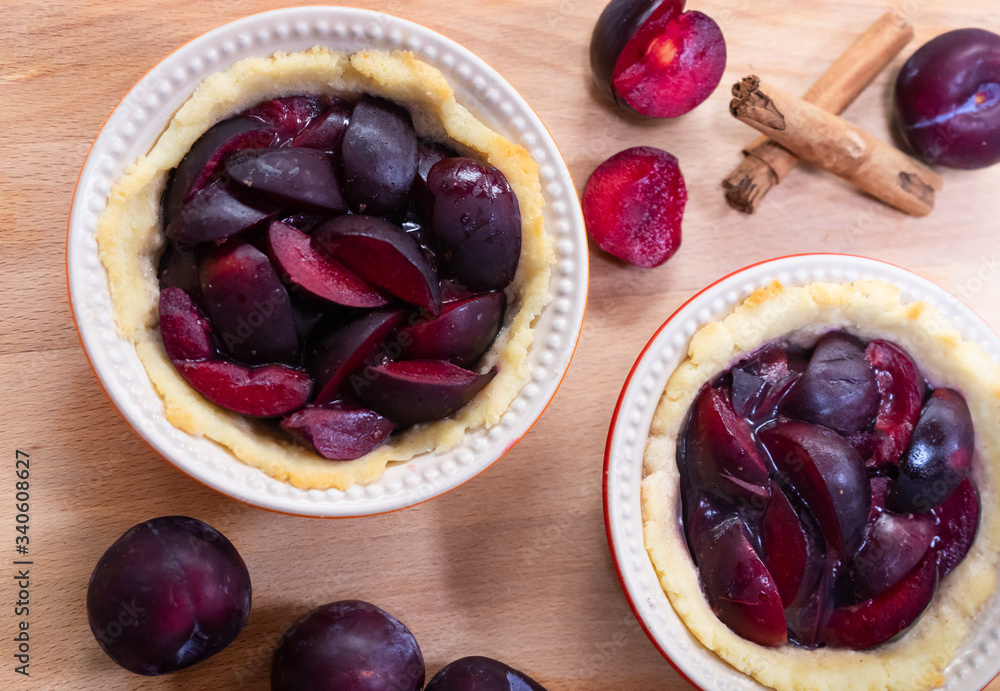 Traditional German glazed plum tartelettes in miniature pie dishes with cinnamon sticks Traditional German glazed plum tartelettes in miniature pie dishes with cinnamon sticks