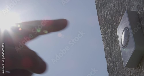 Ringing Doorbell with Protective Gloves and without Male and Female Fingers with Sun Flares and Blue Sky a Concept of Covid-19 Coronavirus Protection
