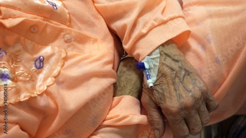 Cannula placed in the wrinkled hand of an elderly patient In hospital bed. Close up