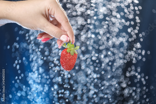 woman hand close up holding red strawberry under drops of water. Girl showing red strawberry on a water background. Healthy lifestyle. Multivitamin cocktail.   Summer diet. 