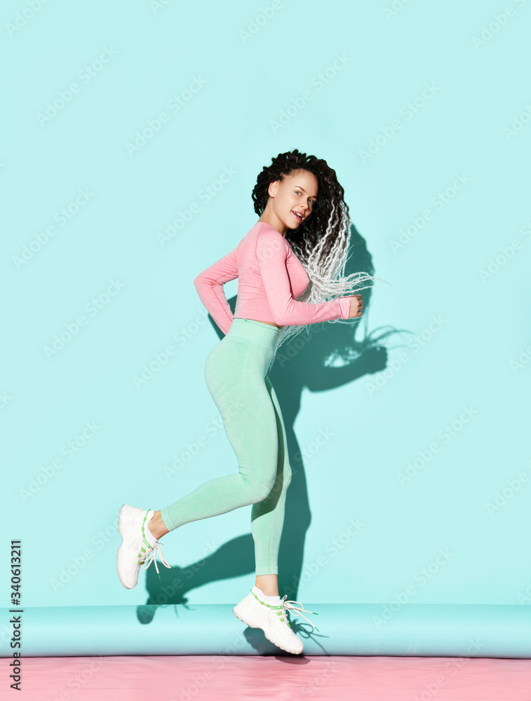 Young beautiful happy girl with dreadlocks hairstyle in sexy sportswear and white sneakers running and smiling