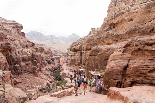 Travelers and tourists climb the impressive staircase carved into the rock that leads to the monastery of Petra.
