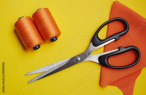 Sewing supplies scissors and spools with orange thread on a yellow tailor table in a workshop. View from above. Close-up