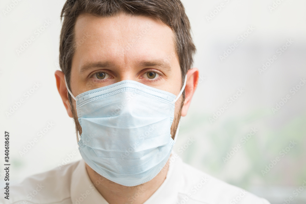 Young male doctor isolated on light gray background. Respirator mask for mouth and nose covering in virus quarantine time. First protection. Healthcare concept. Close up. Front view. Young male doctor isolated on light gray background. Respirator mask for mouth and nose covering in virus quarantine time. First protection. Healthcare concept. Close up. Front view.