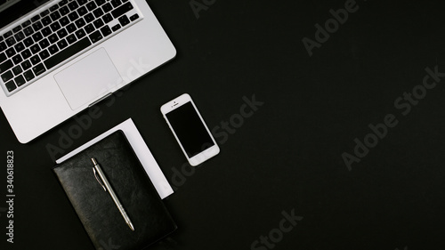 Modern minimalistic workspace with laptop, black leather notebook, smartphone and pen on the black desk. Flat lay, copy space, top view