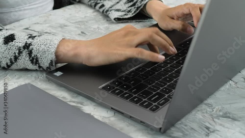 Young caucasian woman's hands typing on the keyboard of laptop, real time video, grey color spectrum, grey background, natural light, office working, freelance, actual lifestyle