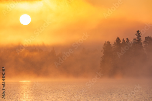 Sun rising above forest and misty lake  Sweden.