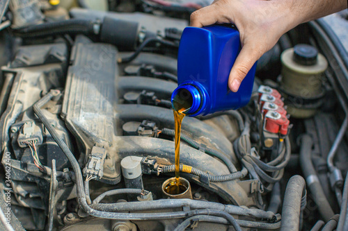 Photo of a male hand pouring an oil into a car engine.